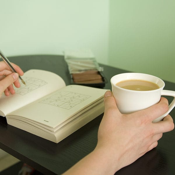 Someone doing a sudoke with a cup of tea and chocolate biscuits