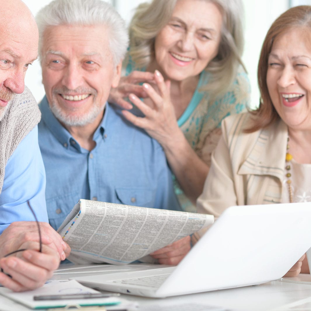 Two Senior Couples Sitting At Table And Working With Laptop